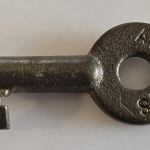 May include: A vintage metal key with a circular head and a rectangular bit. The head is stamped with the letters "ATSF R/S". The key is a dark, aged color, suggesting it is old.