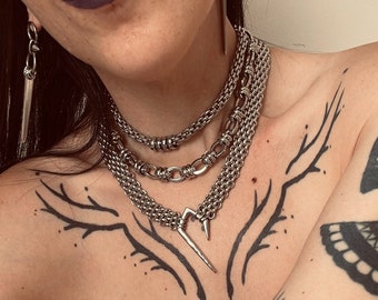 May include: A close-up of a person's chest with multiple silver chain necklaces. The person has several tattoos, including a large beetle with wings on their arm.