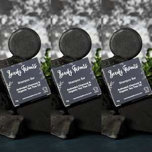 May include: Three black shampoo bars with the text "Beauty Favours" and "Shampoo Bar Activated Charcoal & Organic Tea Tree Oil" on the packaging. The bars are sitting on a black surface.