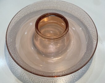May include: A vintage pink glass serving dish with a central, raised circular section. The outer rim features a delicate, etched floral pattern. The dish is likely used for serving food or as a decorative piece.