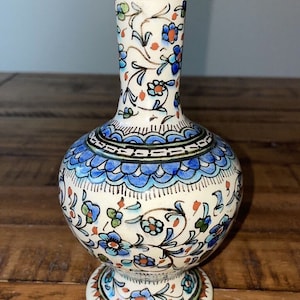 May include: A white ceramic vase with a blue and red floral pattern. The vase has a round body and a narrow neck.