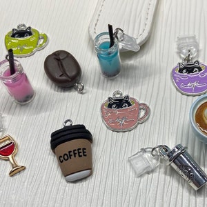 May include: Assortment of colorful charm pendants featuring coffee cups, a wine glass, a coffee to-go cup, and a boba tea. Some of the charms feature a black cat design.
