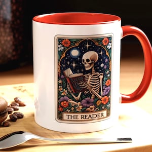 May include: White ceramic mug with a red rim and handle. The mug features a colorful illustration of a skeleton reading a book with the text "The Reader" at the bottom.