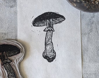 May include: Black and white linocut print of a mushroom with a wide cap and a thick stem.