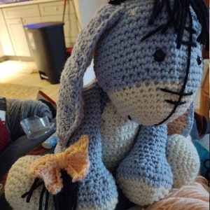 May include: A crocheted blue and white stuffed donkey with a black yarn tail and mane. The donkey has a small orange bow on its back.