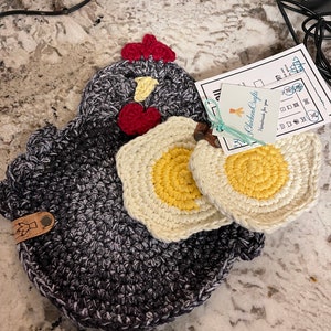 May include: Crocheted black and white chicken pot holder with two crocheted yellow and white egg pot holders. The egg pot holders have a yellow center. The chicken pot holder has a red comb and wattle. The tag reads "Chicken Cafe Handmade for you".