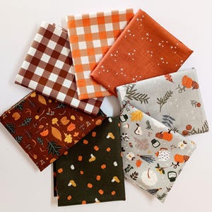 May include: A set of six fabric squares featuring various autumnal patterns. The patterns include a brown and white gingham, an orange and white gingham, a solid orange with white dots, a gray with brown leaves and berries, a brown with orange leaves and berries, and a green with orange dots.
