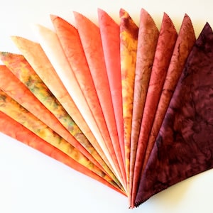 May include: A collection of 17 fabric squares in shades of orange, red, and brown. The fabric squares are arranged in a fan shape, with the lightest colors at the top and the darkest colors at the bottom.