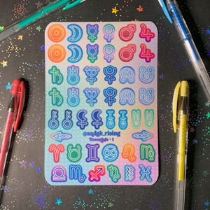 May include: A rectangular sticker sheet featuring a grid of colorful astrological and planetary symbols in gradient hues. The center text reads @sadge_rising Essentials + 1. The stickers are arranged in rows on a light-colored background with a subtle dot pattern.