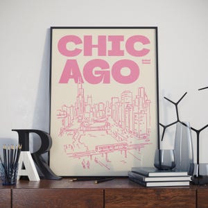 Op de afbeelding: Een ingelijste wandkunstprint met een roze lijntekening van de skyline van Chicago op een cr&egrave;mekleurige achtergrond. De tekst CHICAGO staat in grote roze letters bovenaan, met United States in kleinere roze letters onder de stadsnaam.