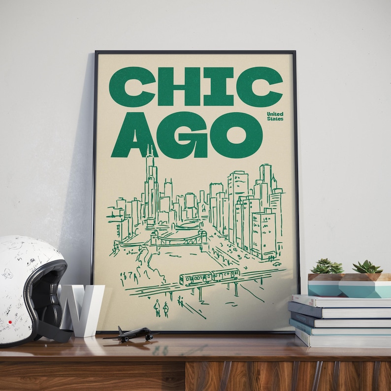 Op de afbeelding: Een ingelijste poster met de tekst CHICAGO en United States in donkergroene inkt op een cr&egrave;mekleurige achtergrond. Het kunstwerk toont een lijntekening van de skyline van Chicago, een rivier met een brug en een verhoogd treinspoor met een trein.