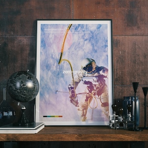 May include: A framed poster with a blue and white background featuring an astronaut in a white spacesuit floating in zero gravity. The poster has the text "zero-gravity" and "Astronaut Edward H. White II" printed on it.