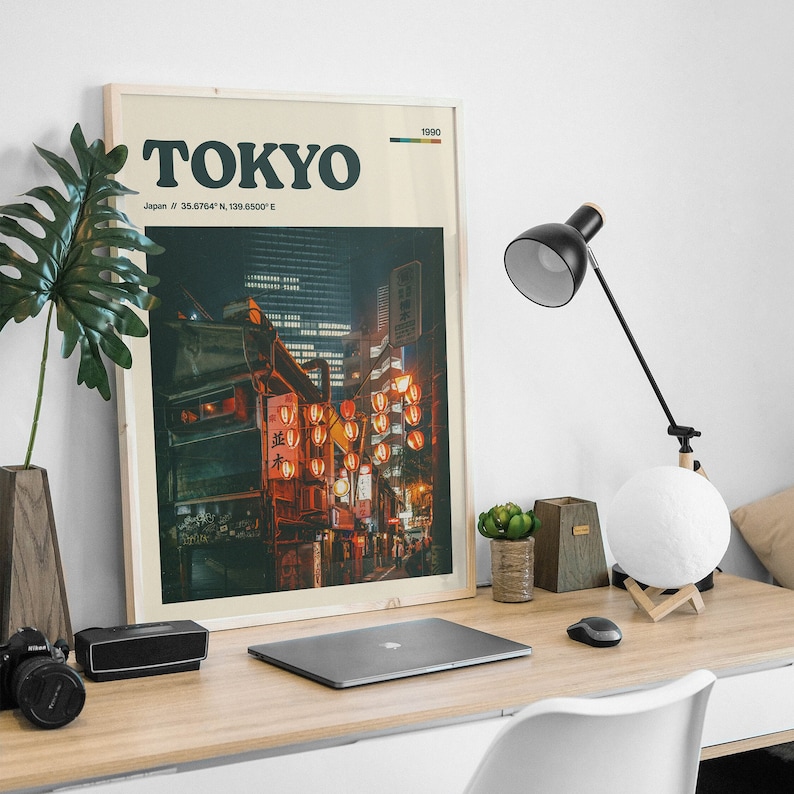 Peut inclure: Une impression encadr&eacute;e &agrave; l'esth&eacute;tique vintage repr&eacute;sentant une vue nocturne de Tokyo, au Japon. L'impression porte le texte "TOKYO" en lettres noires et grasses et les coordonn&eacute;es "35.6764&deg; N, 139.6500&deg; E" en dessous. L'image montre une rue bord&eacute;e de b&acirc;timents et de lanternes rouges.