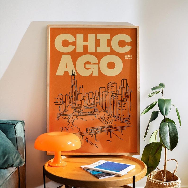 Op de afbeelding: Een ingelijste verticale poster met een feloranje achtergrond en de tekst CHICAGO en United States in cr&egrave;me. Een zwarte lijntekening toont de skyline van Chicago, een brug en een verhoogd treinspoor in het onderste gedeelte.