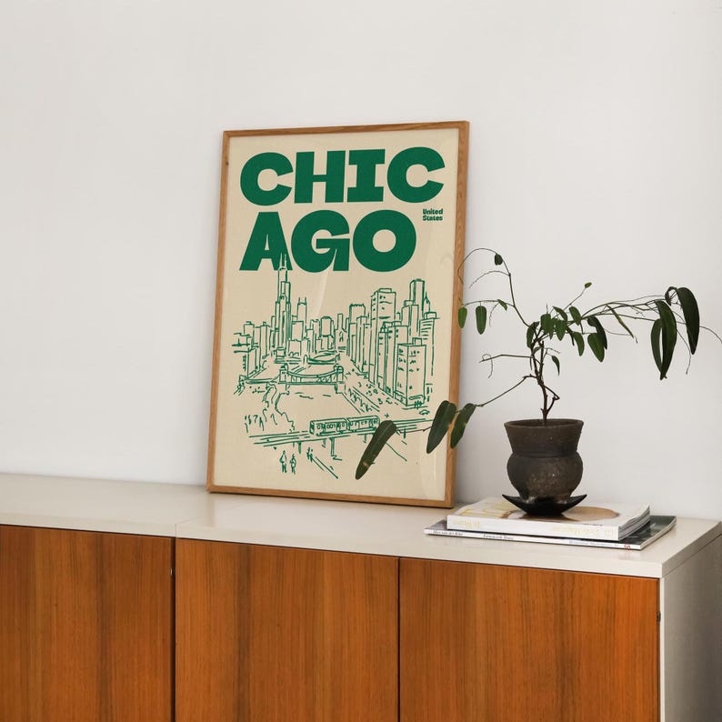 Op de afbeelding: Een ingelijste kunstdruk met een cr&egrave;mekleurige achtergrond en het woord CHICAGO in grote groene letters. Onder de tekst staat een groene lijntekening van de skyline van Chicago, inclusief wolkenkrabbers, een brug, een trein en de tekst United States.