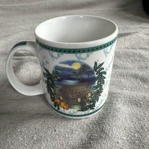 Peut inclure: Un mug en céramique blanche orné d'une scène tropicale avec une hutte au toit de chaume, des palmiers, un soleil jaune et des fleurs d'hibiscus orange. Le motif est encadré par des feuilles vertes et une bordure à pois bleu sarcelle.