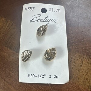 May include: Three gold-toned metal buttons shaped like leaves, attached to a white rectangular display card. The card features the text 4357, Boutique, and F20-1/2" 3 On. Each button has a textured, veined surface and measures 1/2 inch in size.