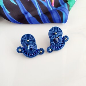 Könnte beinhalten: Ein Paar blaue Ohrringe mit einem Wirbeldesign und einem blauen Kristall in der Mitte.