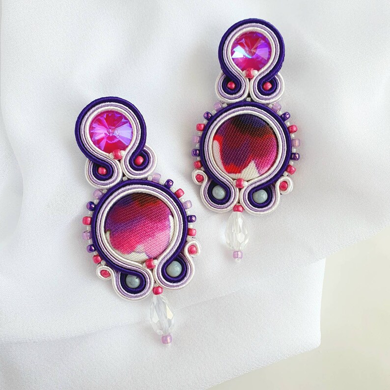 May include: A pair of purple and white earrings with pink and white fabric centers and clear crystal accents.