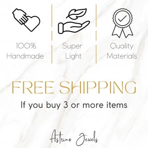 May include: Illustration of three icons representing the benefits of buying handmade jewelry. The first icon shows a hand holding a heart with the text "100% Handmade". The second icon shows a hand holding a leaf with the text "Super Light". The third icon shows a medal with a checkmark and the text "Quality Materials". The text "FREE SHIPPING" is displayed in gold letters below the icons. The text "If you buy 3 or more items" is displayed in black letters below the "FREE SHIPPING" text. The text "Astrine Jewels" is displayed in black cursive letters below the previous text.