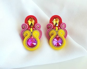 May include: A pair of colorful earrings with pink, yellow, and red accents. The earrings feature a large, clear crystal in the center and smaller crystals around the edges.