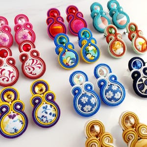 May include: Assortment of colorful fabric earrings with various patterns and embellishments. The earrings are made with multiple layers of fabric and feature a variety of colors, including blue, red, yellow, green, and pink.
