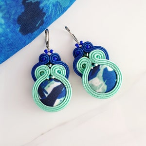 Könnte beinhalten: Ein Paar blaue und grüne Ohrringe mit einem Spiraldesign und einem blauen und weißen Stoffzentrum.