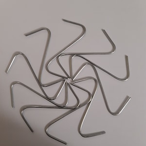 Op de afbeelding: Een set van tien zilveren metalen haken die in een cirkelvormige opstelling op een witte achtergrond zijn gerangschikt.