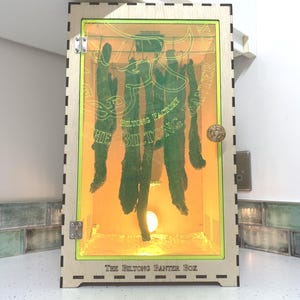 May include: A wooden box with a glass door and a light inside. The box is labeled "The Biltong Banter Box" and has a green bull logo with the text "Biltong Factory".