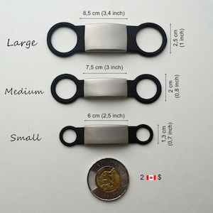 May include: Three sizes of black silicone dog tags with silver metal plates. The tags are shown next to a Canadian two dollar coin for size comparison. The tags measure 8.5 cm (3.4 inches), 7.5 cm (3 inches), and 6 cm (2.5 inches) in length. The tags are labelled "Large", "Medium", and "Small".
