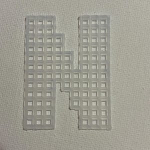 May include: A translucent white plastic canvas letter "N" with a grid-like pattern. The letter is cut out, with a section missing from the middle. The background is a plain white surface.