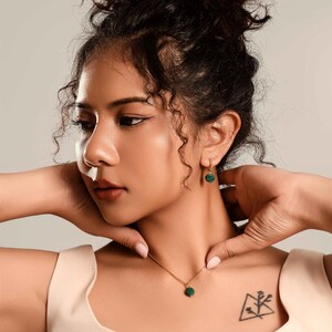 Peut inclure: Un collier en or et une paire de boucles d'oreilles assorties avec de petits pendentifs ronds en pierre verte. Le bijou est port&eacute; par une personne aux cheveux fonc&eacute;s. L'ensemble est assorti.