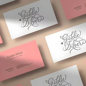 Pu&ograve; includere: Un set di biglietti da visita rosa e bianchi con il testo "Goldie Silver" e "Wedding Planner" in caratteri neri. I biglietti sono disposti in modo sparso su una superficie marrone chiaro.