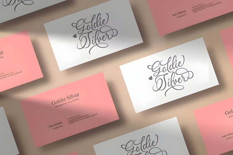 Pu&ograve; includere: Un set di biglietti da visita rosa e bianchi con il testo "Goldie Silver" e "Wedding Planner" in caratteri neri. I biglietti sono disposti in modo sparso su una superficie marrone chiaro.