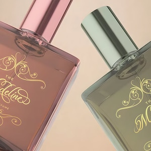 Pu&ograve; includere: Due flaconi di profumo in vetro con scritta dorata "The Madeline Eau de Perfume". I flaconi hanno un design decorativo dorato e sono su uno sfondo beige.