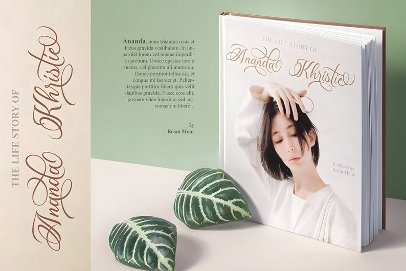 Pu&ograve; includere: Un libro bianco con il titolo "The Life Story of Ananda Khristie" in un font corsivo. Il libro &egrave; aperto per rivelare una foto di una donna con capelli neri corti. Il libro &egrave; appoggiato su una superficie bianca con due foglie verdi.