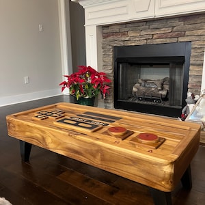 Op de afbeelding: Een houten salontafel in de vorm van een vintage videogamecontroller. De tafel heeft zwarte poten en rode knoppen met de labels "A", "B", "R" en "Start".