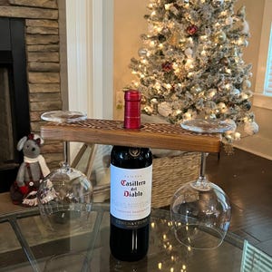 May include: Wooden wine bottle and glass holder with a carved Celtic knot design. The holder is holding a bottle of Casillero del Diablo Cabernet Sauvignon wine and two wine glasses.