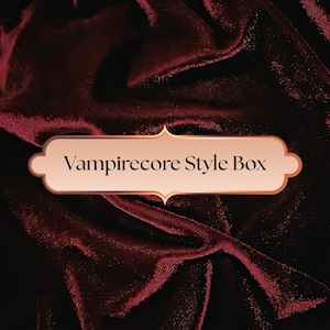 May include: A burgundy velvet fabric background with a decorative, light brown and gold-edged label. The label reads "Vampirecore Style Box" in a serif font, suggesting a themed product.