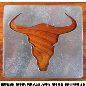May include: A metal cutout of a bull's head with horns, set against a wooden background. The text "ALL ITEMS MADE IN AMERICA" is at the top. The cutout is in a rectangular shape.