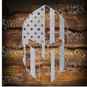 May include: A silver metal Spartan helmet with an American flag design. The helmet is against a wood background.