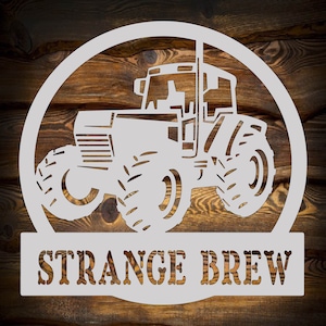 May include: White silhouette of a tractor with the text "STRANGE BREW" below it. The tractor is inside a white circle on a brown wooden background.