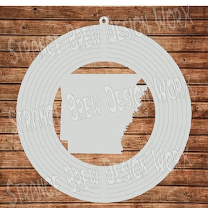 May include: A gray metal wind spinner with a circular design. The center of the spinner features a silhouette of the state of Arkansas.