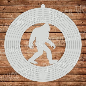 Peut inclure: Une silhouette grise de Bigfoot marchant, à l'intérieur d'un motif circulaire avec des cercles concentriques, ressemblant à un carillon.