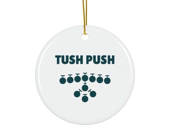 May include: White ceramic ornament with the text "TUSH PUSH" in dark teal. Below the text are teal circles arranged in a pattern. A gold string is attached for hanging.