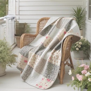 May include: A patchwork quilt featuring a variety of square fabric blocks in shades of gray, white, and beige. The quilt displays alternating patterns including small floral prints, gingham checks, and solid textures, draped over a wicker chair.