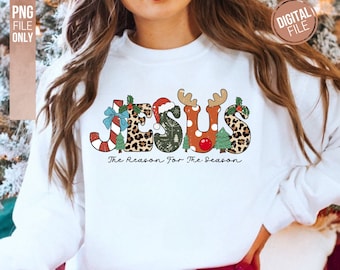 May include: A white long-sleeve sweatshirt featuring the word JESUS in a multi-patterned design with candy cane, leopard print, forest green, polka dot, and reindeer antler motifs, with the text The Reason For The Season printed below.