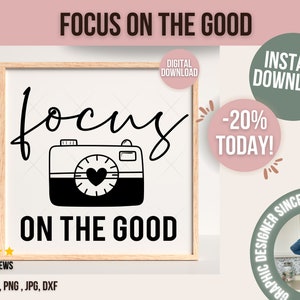 May include: A black and white digital illustration of a camera with a heart in the viewfinder. The text "focus on the good" is written in a cursive font above and below the camera.