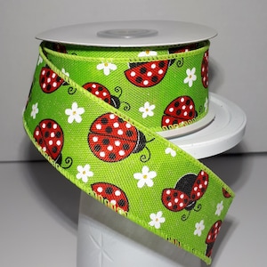 May include: Green ribbon with a white daisy and red ladybug print. The ribbon is on a spool.