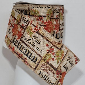 May include: A roll of beige and gold ribbon with an autumn theme. The ribbon features a repeating pattern of leaves, berries, and the words "Fall" and "Autumn".